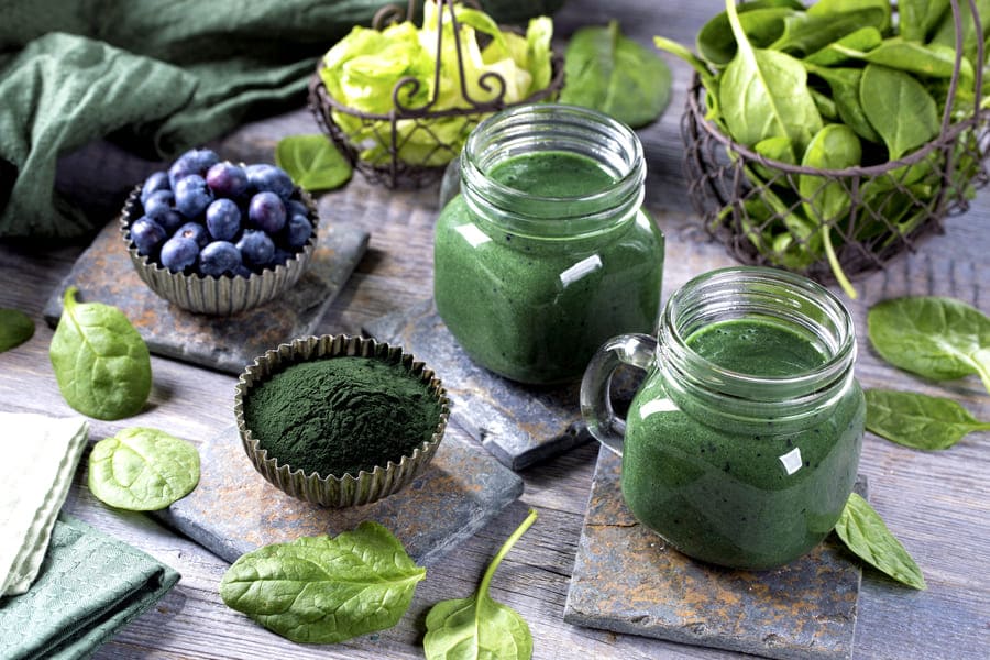 spirulina-bogati-kolagen-hrani Богати на колаген храни. Дефицит на желязо. Маса със купичка от спирулина, разбпръснат спанак и боровинки