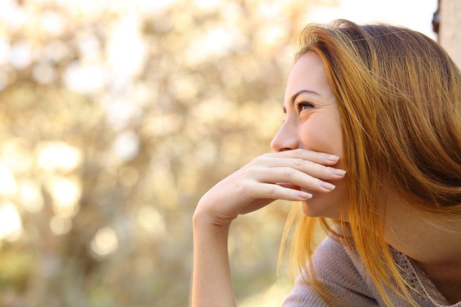 Happy woman laughing covering her mouth with a hand with a warmth background