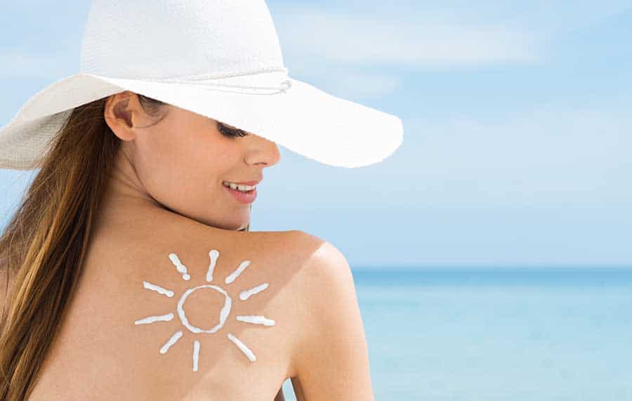 Млада жена гледа към гърба си, където има нарисувано слънце от слънцезащитен продукт. 