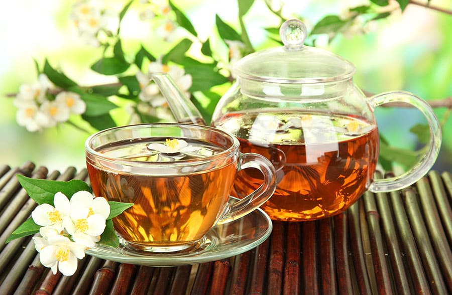 Зелено кафе за отслабване. Намаляване на апетита. Фитонутриенти. Чаша и кана с чай за отслабване, разположени на дървена маса в красива градина.