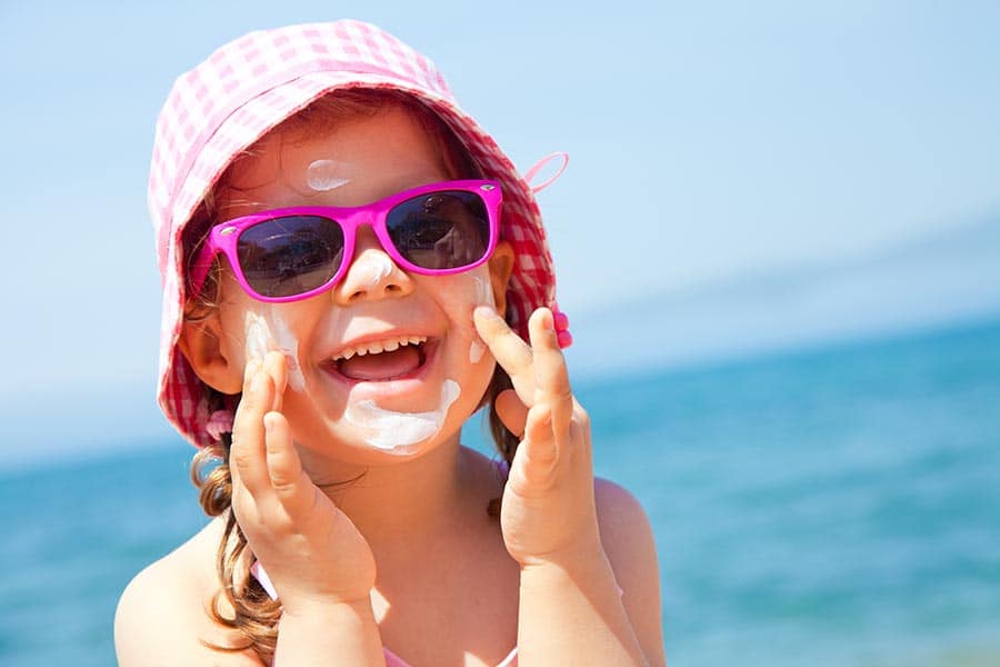 Малко момиченце на плажа нанася слънцезащитен крем на лицето си 