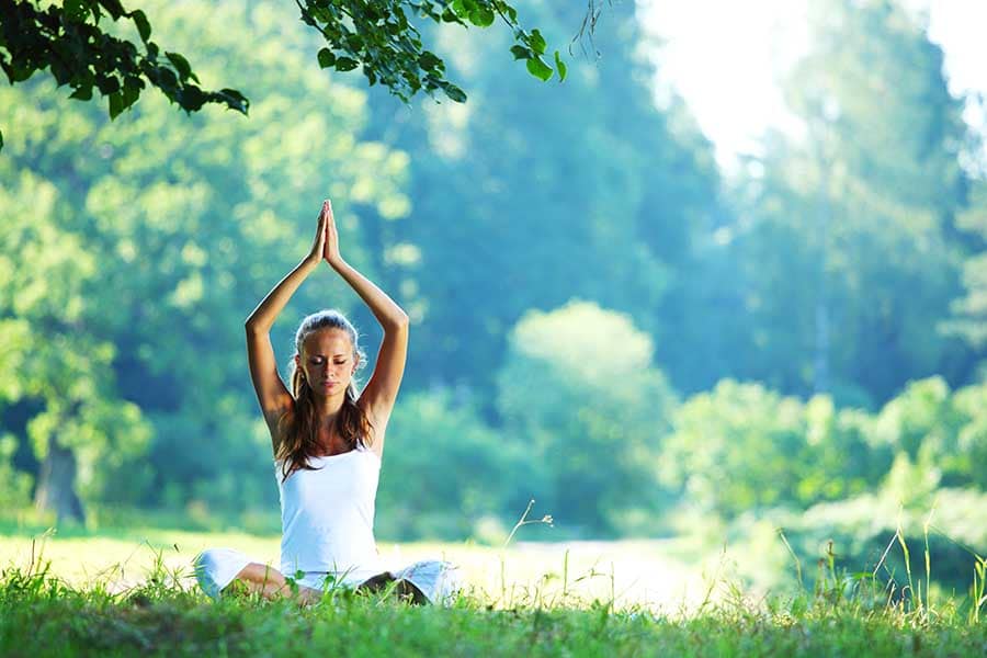 Жена, практикуваща йога върху зелена трева, в поза лотус. Част от упражнения по време на кетоза.