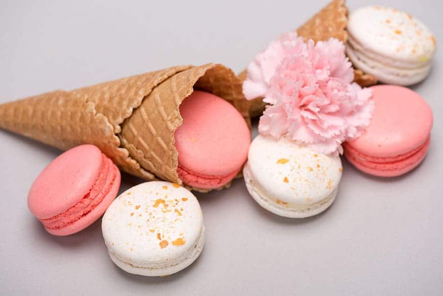 Вредни храни. Видове захари. Дизахариди. Бисквитена фуния за сладолед, напълнена с френски макарони - тип сладки в различни цветове.
