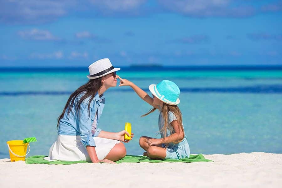 Факти за вигтамин Д. Биотин през лятото. Витамини за лятото. Малко момиченце маже носа на майка сис ъс слънцезащитен продукт на плажа.
