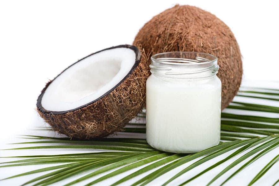 Кокосов орех и буркан с кокосово масло, поставени върху палмово листо.