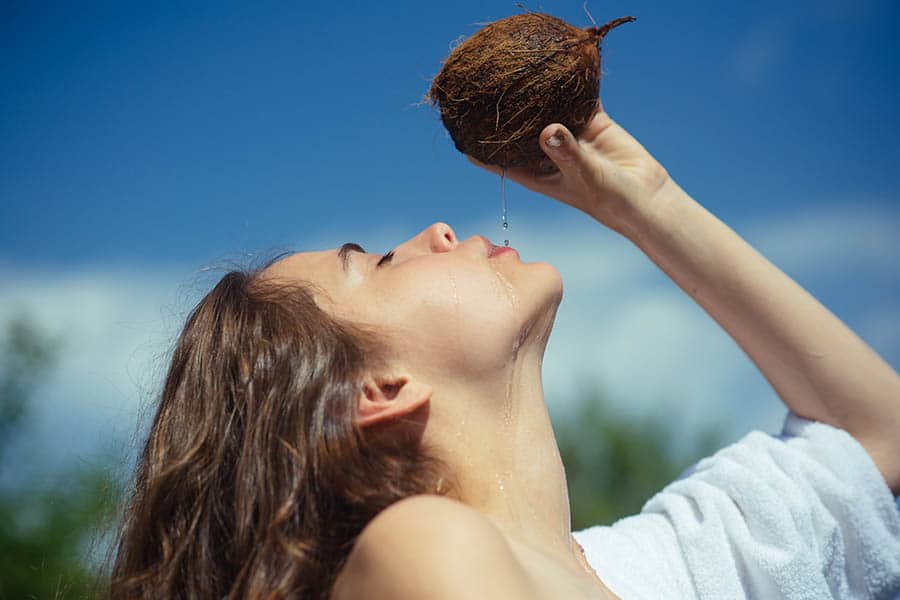 Витамини за лятото. Млада жена пие от кокосов орех на плажа.