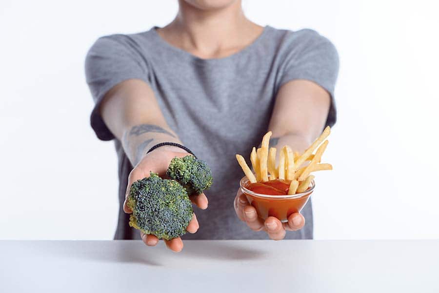 Веган кето диета. Жена, която показва броколи и пържени картофи - изборът на правилната храна за добрия холестерол