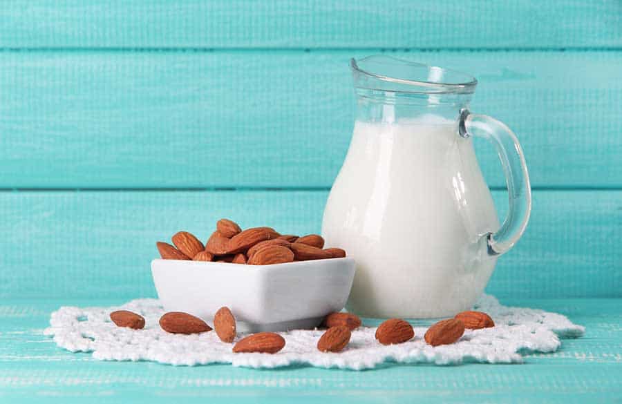 Almond milk in jug with almonds in bowl, on color wooden background