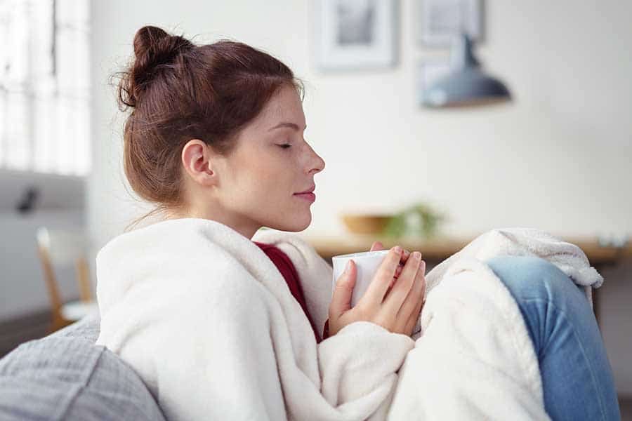 Златно мляко. woman holding a cup of warm tea while relaxing on the sofa with eyes shut