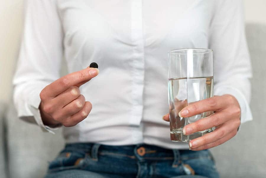 Woman’s hand holding activated carbon pills. За какво се използва активен въглен.