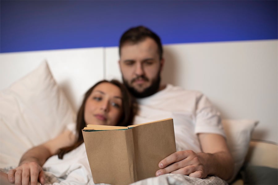 Двойка чете книга в леглото - един от съветите при трудно заспиване